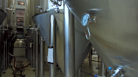 slow pan right from large stainless steel beer fermentation tanks in a brewery to a close shot of a pressure gauge