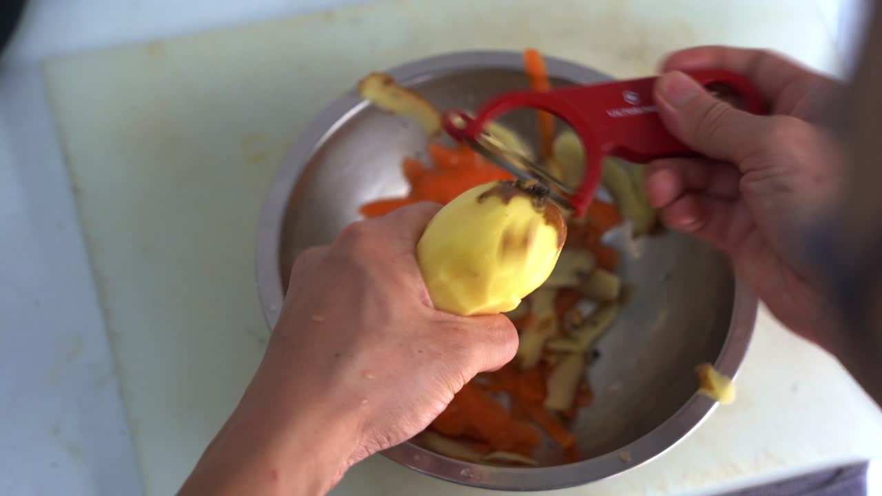 Vista dall'alto che riprende un addetto alla cucina che pela una patata con un pelapatate, preparazione per le operazioni del ristorante