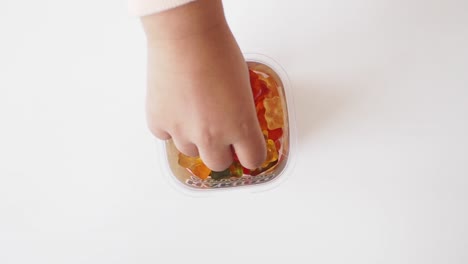 child's hand reaching for gummy bears in a container