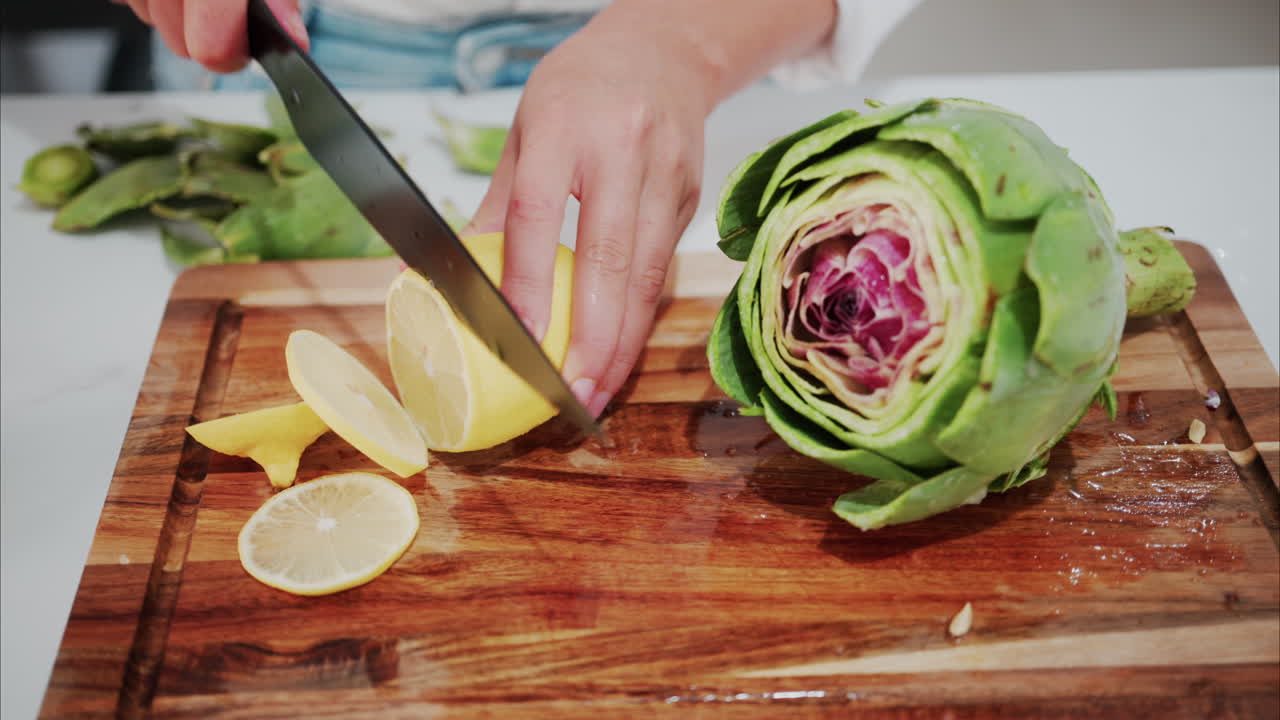 Woman cutting up a lemon near an artichoke on a wooden cutting board