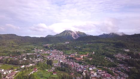 disparo de un dron volador alto que viaja sobre la ciudad de berastagi, el pueblo y el bosque verde con vista al monte sibayak del volcán activo en el norte de sumatera indonesia
