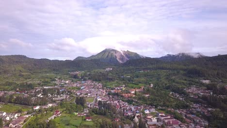 high forward flying drone shot traveling above berastagi town, village and green forest with active volcano mount sibayak view in north sumatera indonesia