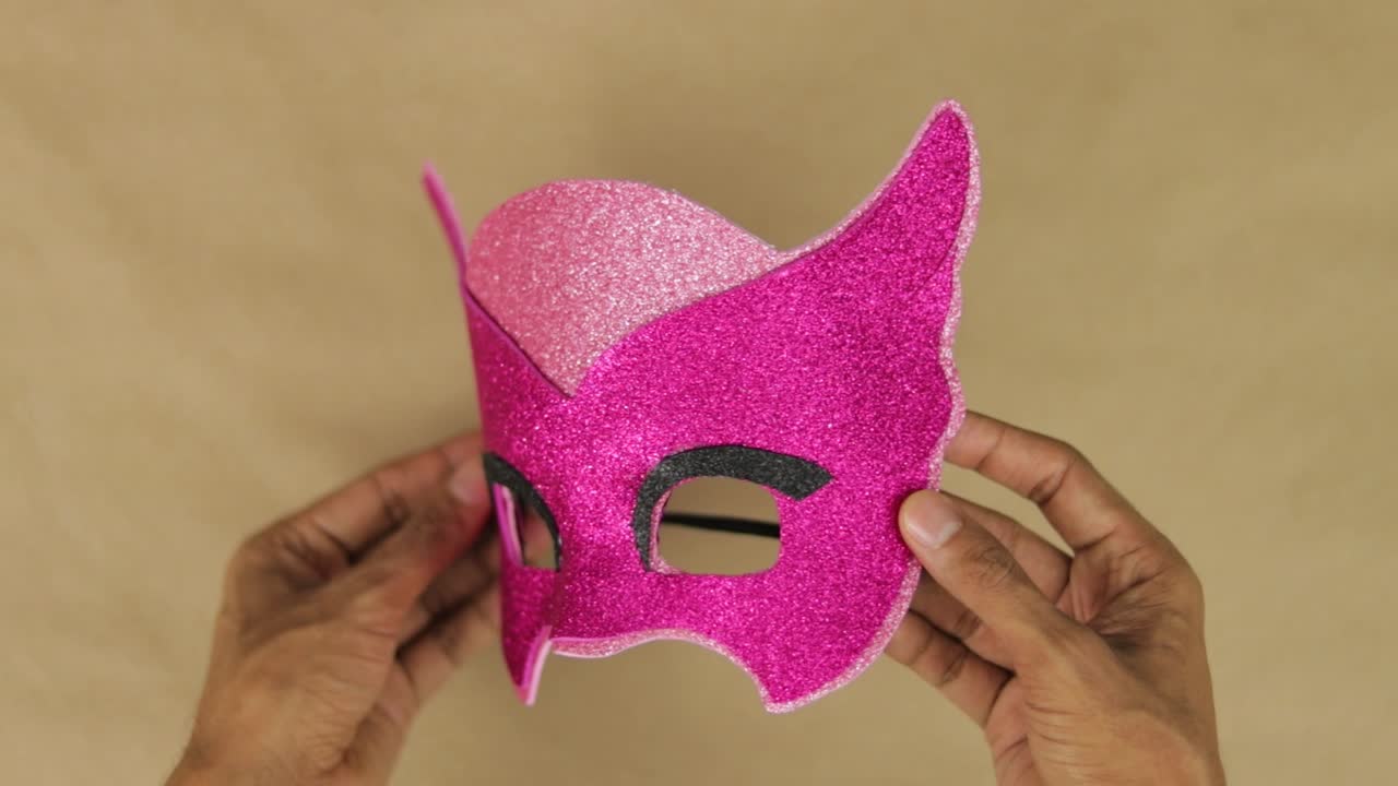 Mãos fazendo máscara da Corujinha com espuma rosa de diamante para o carnaval.