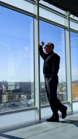 thoughtful adult businessman comes up to a panoramic window. man looks a sunny cityscape from upper floor office. vertical video.