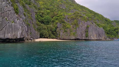 Small-Sandy-Beach-Under-Limestone-Cliffs,-Boat-Passenger-POV-of-Stunning-Coastline-of-El-Nido-Islands-Archipelago,-Philippines