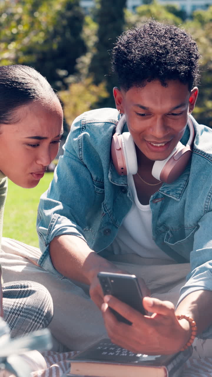 Happy Young Couple Laughing While Looking at Smartphone in Park