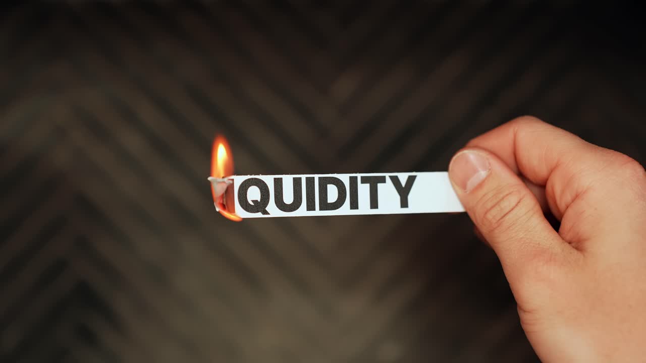 Una mano sostiene una tira de papel con la palabra “LIQUIDEZ” mientras se quema, visualizando la presión del flujo de caja, el riesgo crediticio y el estrés del mercado sobre un fondo oscuro con espacio para texto.