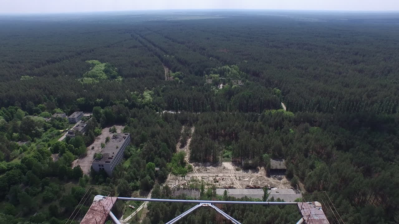 Vista aerea di edifici abbandonati e degradati in una foresta lussureggiante; un complesso industriale dimenticato riconquistato dalla natura.