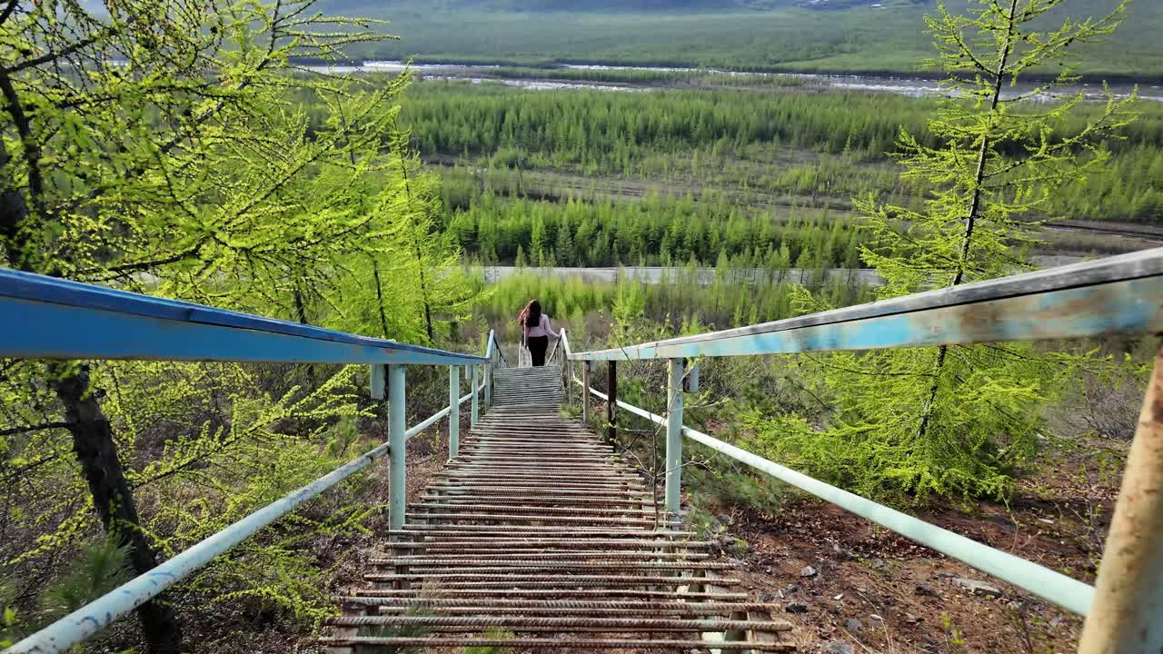 A hiker making their way down a long staircase surrounded by verdant trees and a sweeping landscape on a crisp spring morning.