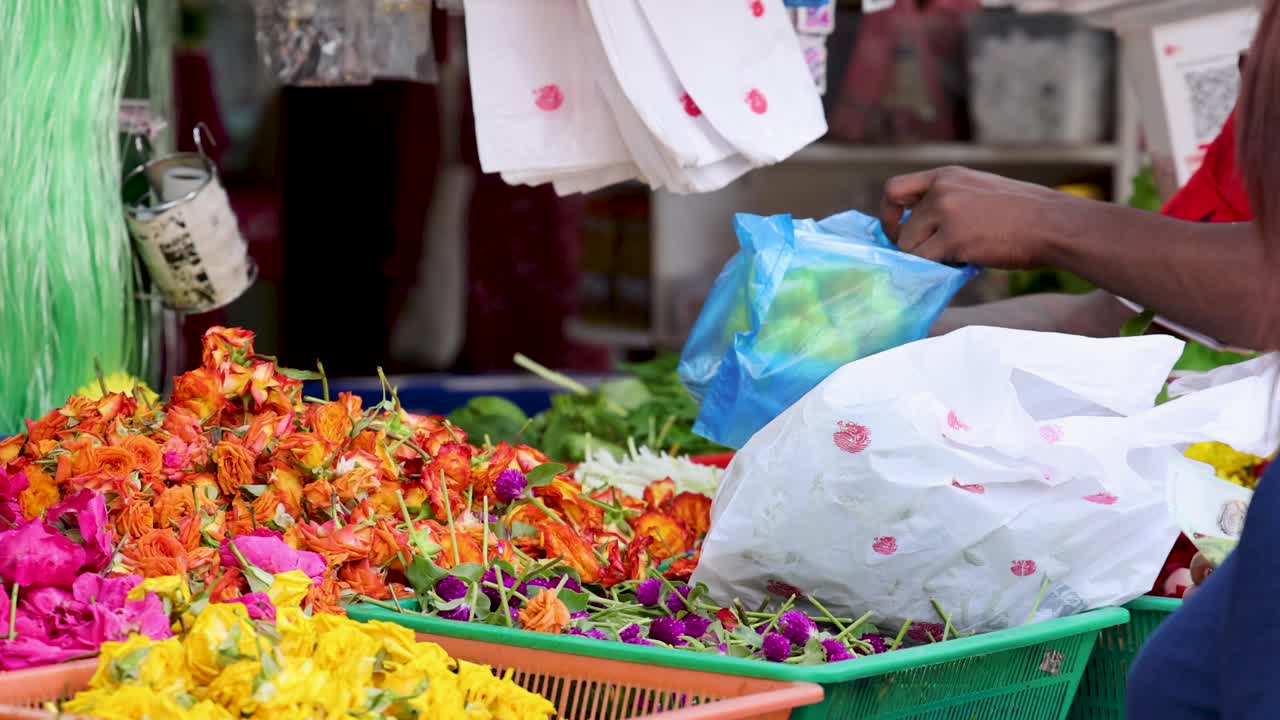 Un vendedor selecciona y empaca vibrantes guirnaldas de flores en una bolsa de plástico en un puesto de mercado al aire libre en Singapur, bajo la brillante luz natural del día.