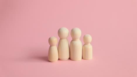 Hands arranging wooden peg dolls on a pink surface, symbolizing family or community building