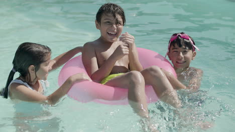 Niños-Felices-Divirtiéndose-Jugando-Con-Un-Anillo-Inflable-En-La-Piscina.