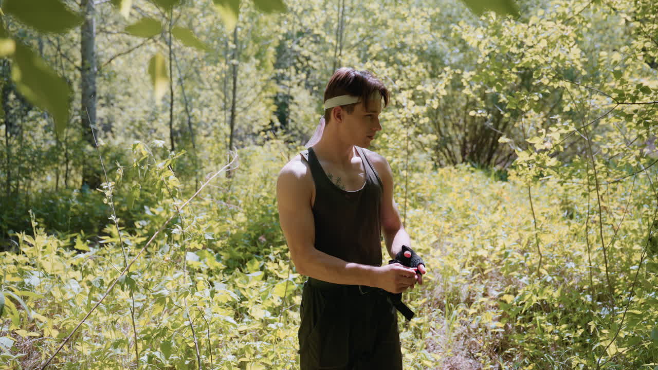 Adventurer pulling off gloves in secluded sunlit forest, sunlight dazzling on shoulders and arms as he adjusts gear amidst dense green foliage and quiet scene, with clear view of trees around