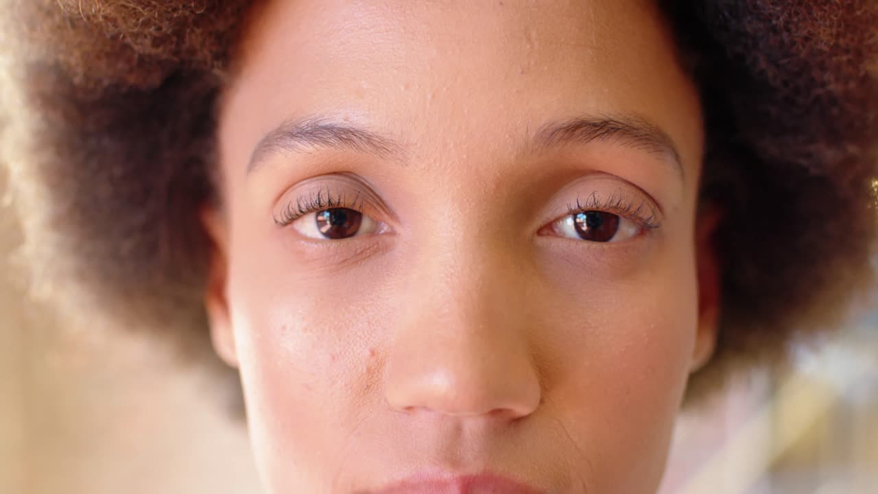retrato en primer plano de una mujer de negocios biracial que abre los ojos, sonriendo en la oficina, en cámara lenta