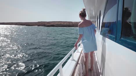 portrait of a young beautiful sexy caucasian woman on a yacht in in a blue dress and sunglasses invites to travel. the concept of vacation, freedom, sunny summer. blue ocean on backgroung. steadycam