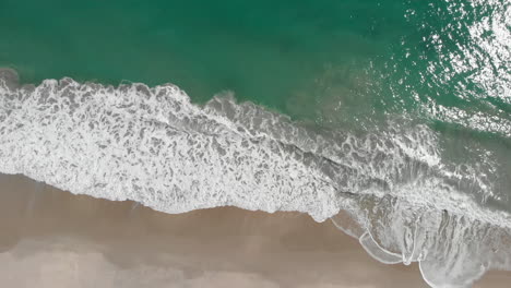 top down aerial view of azure blue water and ocean breaking waves on sandy beach