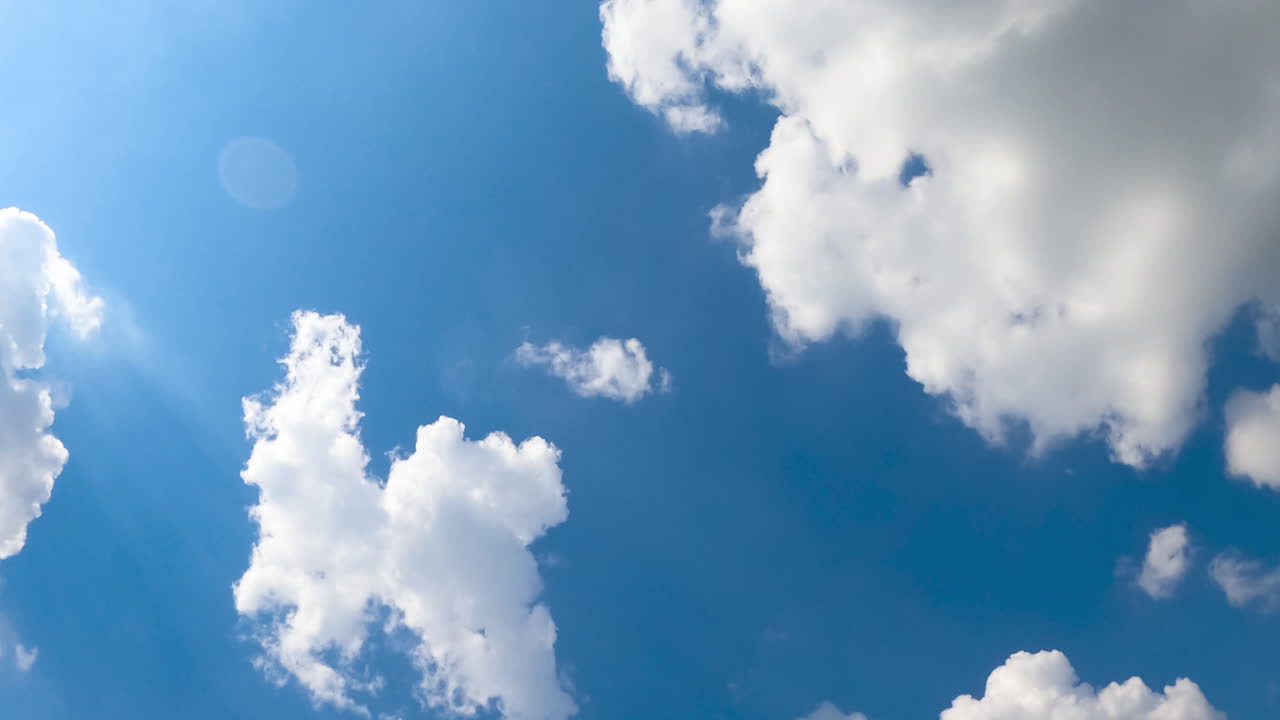Cotton soft clouds flying in the azure sky. Bright sun lighting the clouds. Low angle view. Timelapse.
