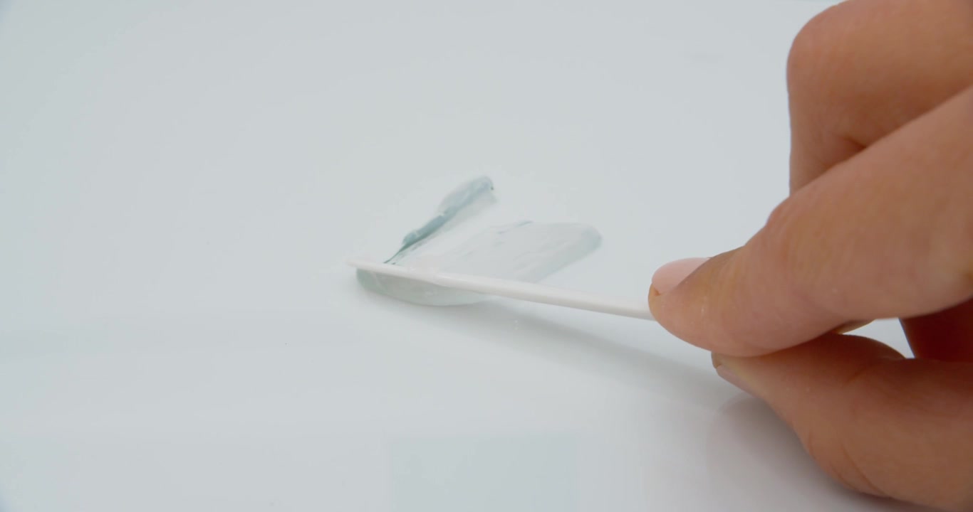Woman's hand stroking transparent gel with spatula on white surface extreme close up view in slow motion.
Organic cosmetic skin care product for wellness and beauty.