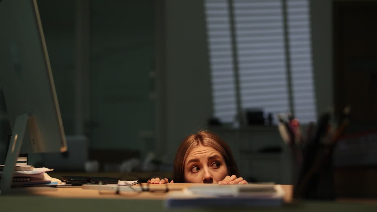 Woman Hiding and Peeking Over Office Desk with Alarmed Expression
