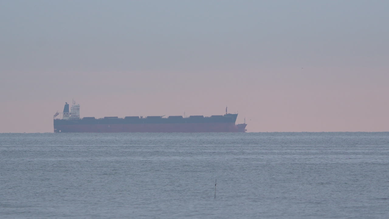 해가 지는 동안 조용한 바다의 거리에서 화물 선박 - 넓은