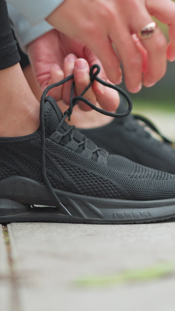 Close-up of lady tightening her black sneakers with golden ring on her finger, preparing for outdoor exercise or workout, focused on footwear and active lifestyle