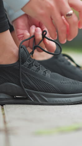 close-up of lady tightening her black sneakers with golden ring on her finger, preparing for outdoor exercise or workout, focused on footwear and active lifestyle
