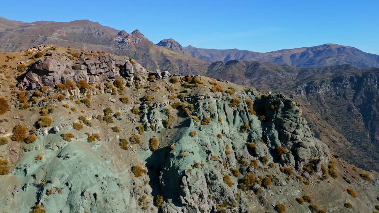 Volo in avanti sopra scogliere erose e colorate con sfondo montuoso.