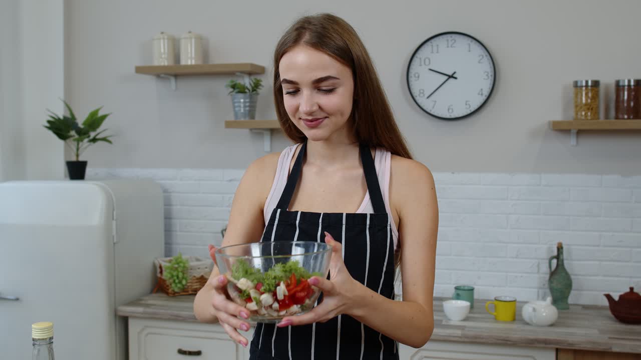 jovem feliz comendo salada de vegetais crus frescos posando na cozinha com emoção positiva
