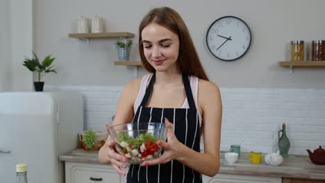 happy young woman eating fresh raw vegetable salad posing at kitchen having positive emotion