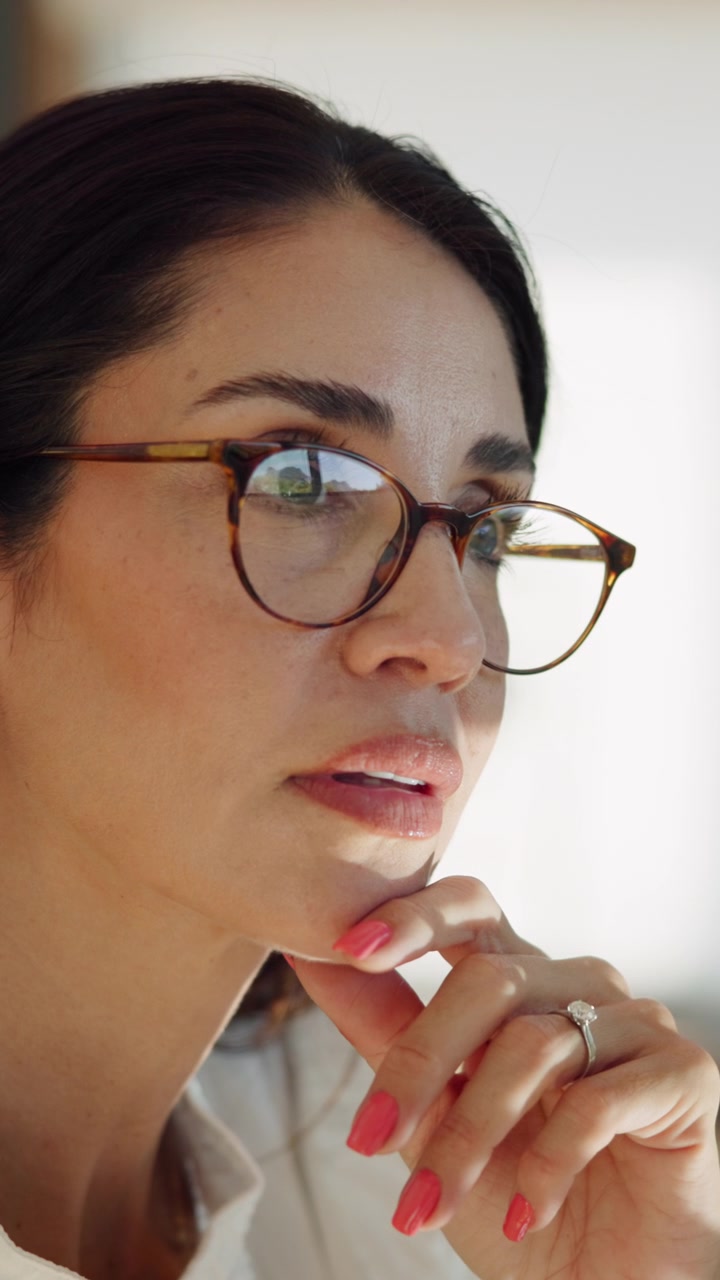 Donna pensierosa con occhiali che guarda verso il basso in un ufficio luminoso