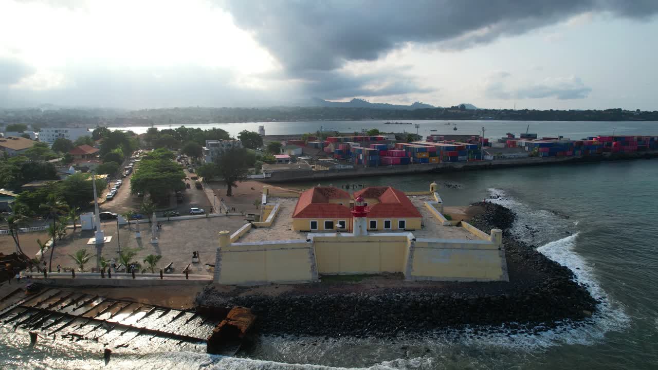 Veduta aerea in arretramento che mostra il faro sopra il forte di São Sebastião, noto anche come Museo Nazionale, con la Baia di Ana Chaves sullo sfondo e la città coperta di nuvole. São Tomé, Africa.