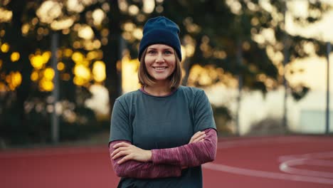 Portrait-of-a-happy-blonde-girl-with-a-bob-hairstyle-in-a-gray-sports-uniform-who-looks-at-the-camera-and-smiles-on-a-street-area-early-in-the-morning-at-sunrise