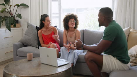 diverse friends chatting on sofa with laptop, enjoying relaxed conversation at home