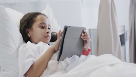 happy biracial sick girl patient using tablet in hospital bed in slow motion