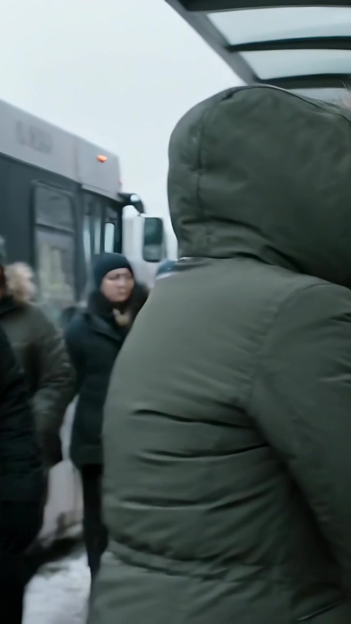 Vertical video: Bracing cold wind person in green parka tugging fur hood on platform to board train
