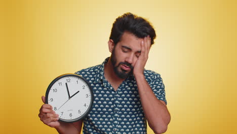 young indian man with anxiety checking time on clock, running late to work, being in delay, deadline