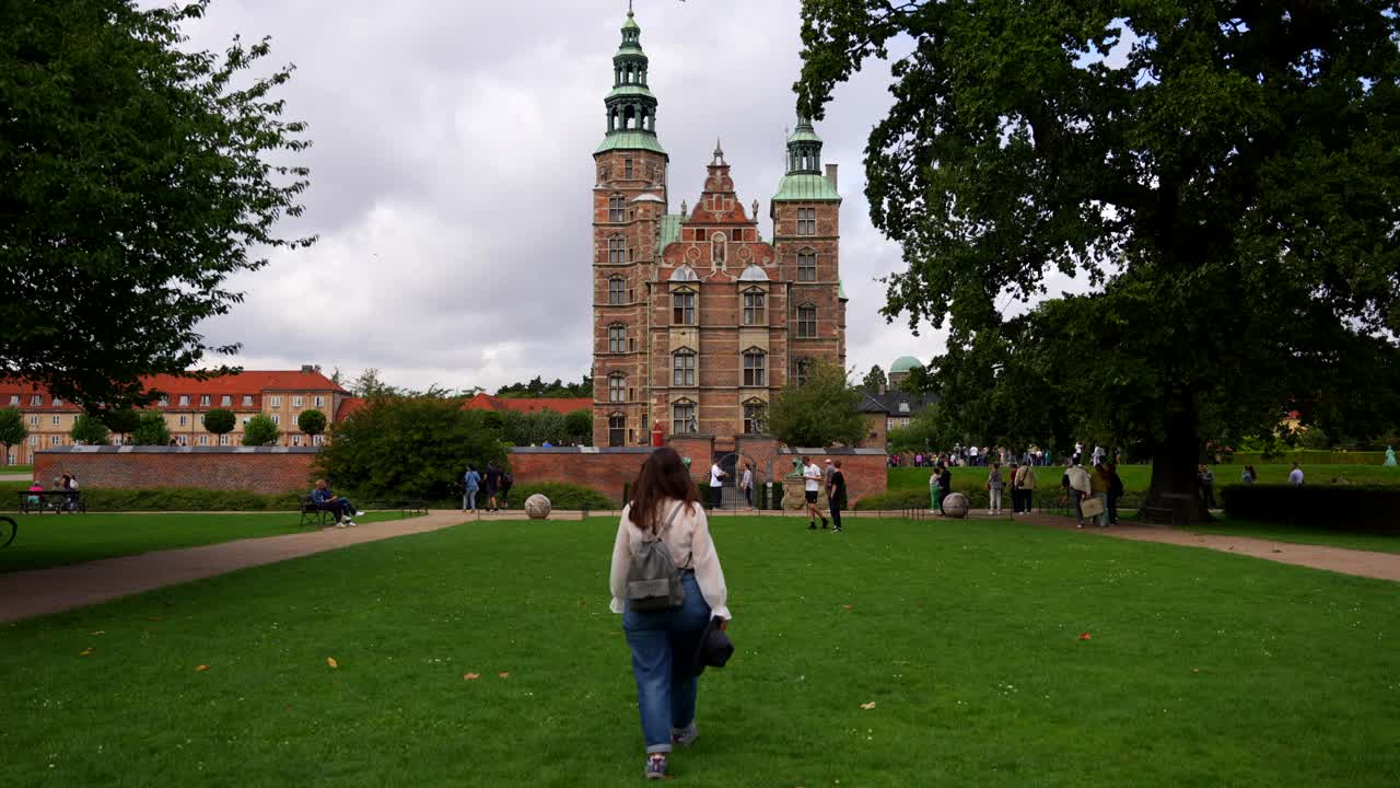 Statisk billede af en kvinde, der går i græsset mod Rosenborg Slot, København.