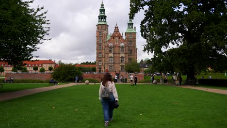 Static-shot-of-a-woman-walking-in-the-grass-towards-Rosenborg-Castle,-Copenhagen