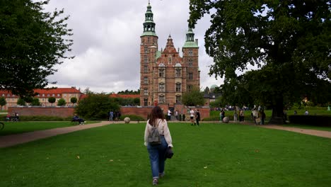 static shot of a woman walking in the grass towards rosenborg castle, copenhagen