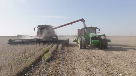 low-angle aerial shot of harvester and tractor: harvest being poured into container