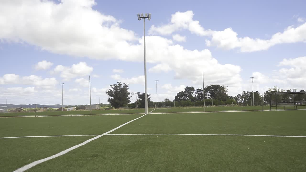 Lush green soccer field basking in sunlight, white lines marking boundaries, under a vibrant blue sky dotted with fluffy white clouds