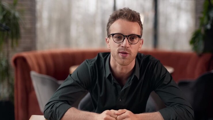 Handsome curly man with glasses talks looking into the camera