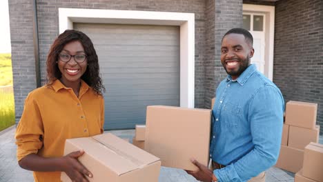 rear view on african american young couple walking in yard at big house and carrying carton boxes