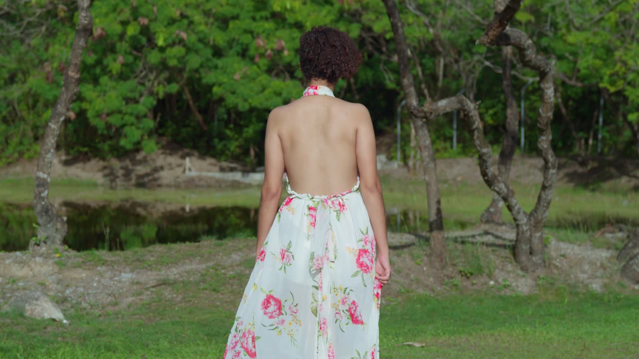 сексуальная девушка со светлой кожей идет к озеру в парке и поворачивается вокруг него, ее платье развевается на ветру