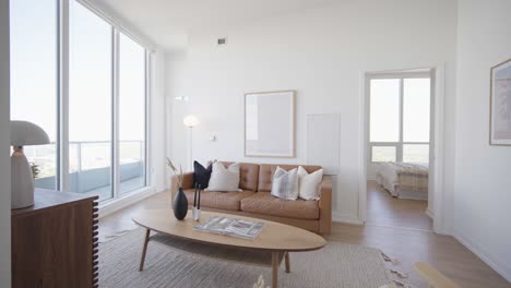 wide angle orbit shot of the living area of a high ceiling penthouse condominium unit with a floor to ceiling window wall at the side and balcony outside during a sunny day