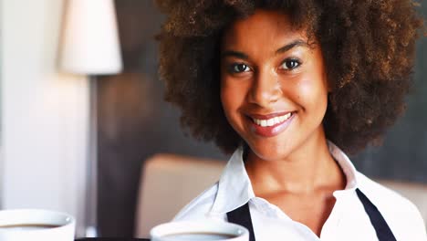 Portrait-of-smiling-waitress-holding-tray-of-coffee-cups-