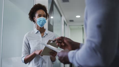 mixed race businesswoman in face mask using digital tablet in office