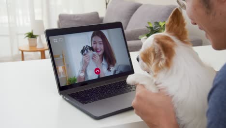 vista por encima del hombro del hombre asiático llamada de video o videoconferencia con la novia y la mascota sentirse feliz.asia pareja saludando por computadora portátil conexión en línea durante el auto-aislación.concepto de amante de mascotas