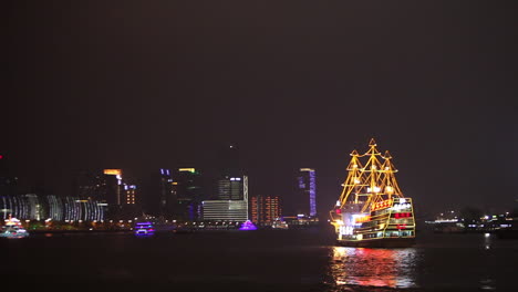 the night skyline of shanghai china with river traffic foreground and illuminated tall ship passing