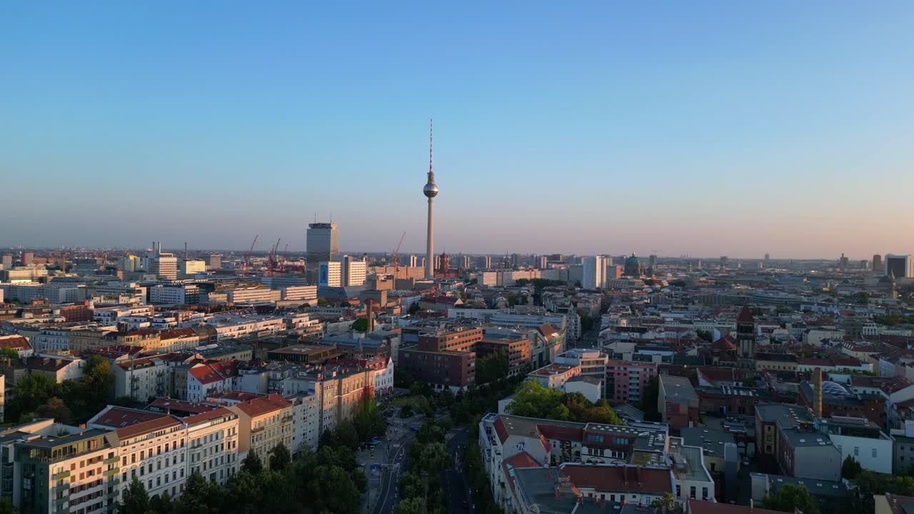 Berlin tv tower rising above rooftops and a construction site at senefelderplatz during sunset. Dramatic aerial view flight descending drone